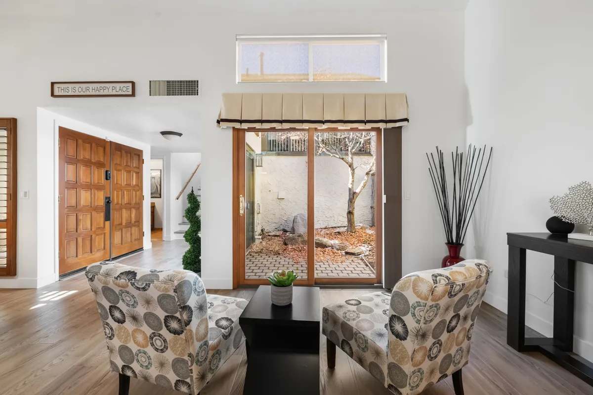 An inviting and serene sitting area featuring comfortable chairs, a coffee table, and large sliding doors that open to views of the garden. Decorative plants and abundant natural light create a peaceful atmosphere ideal for relaxation and enjoying the surrounding pines.