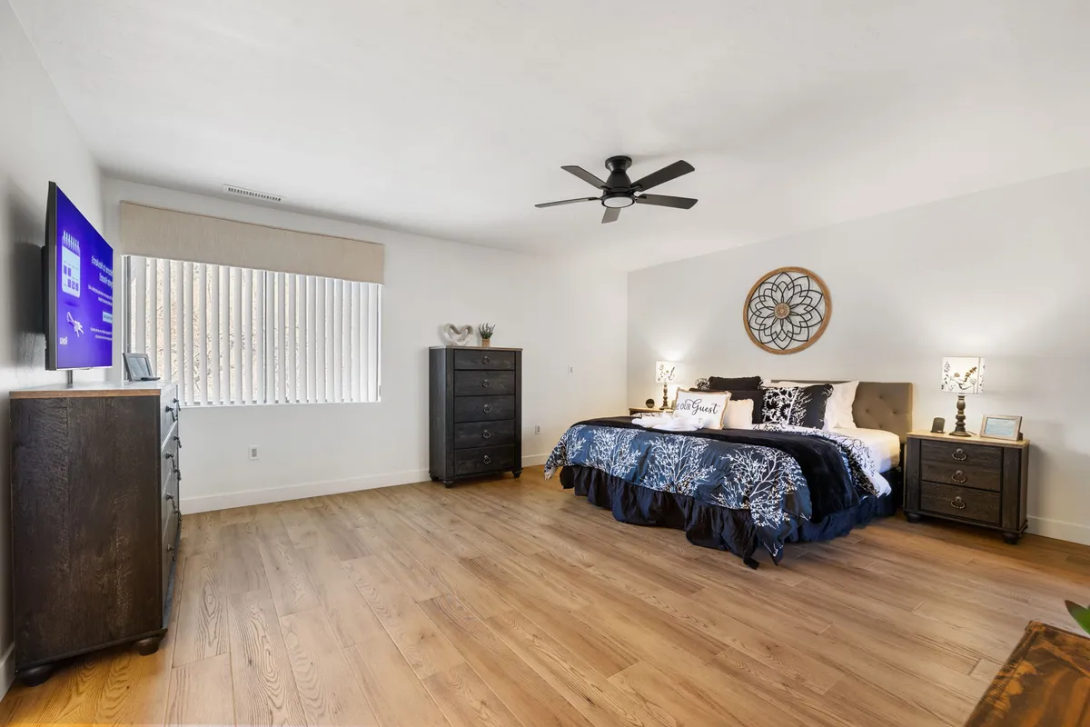 A tranquil bedroom setup featuring a comfortable bed, nightstands, a dresser, and an in-room television. The neutral tones and soft lighting create a restful environment, with features that add to the feeling of privacy and personal retreat.