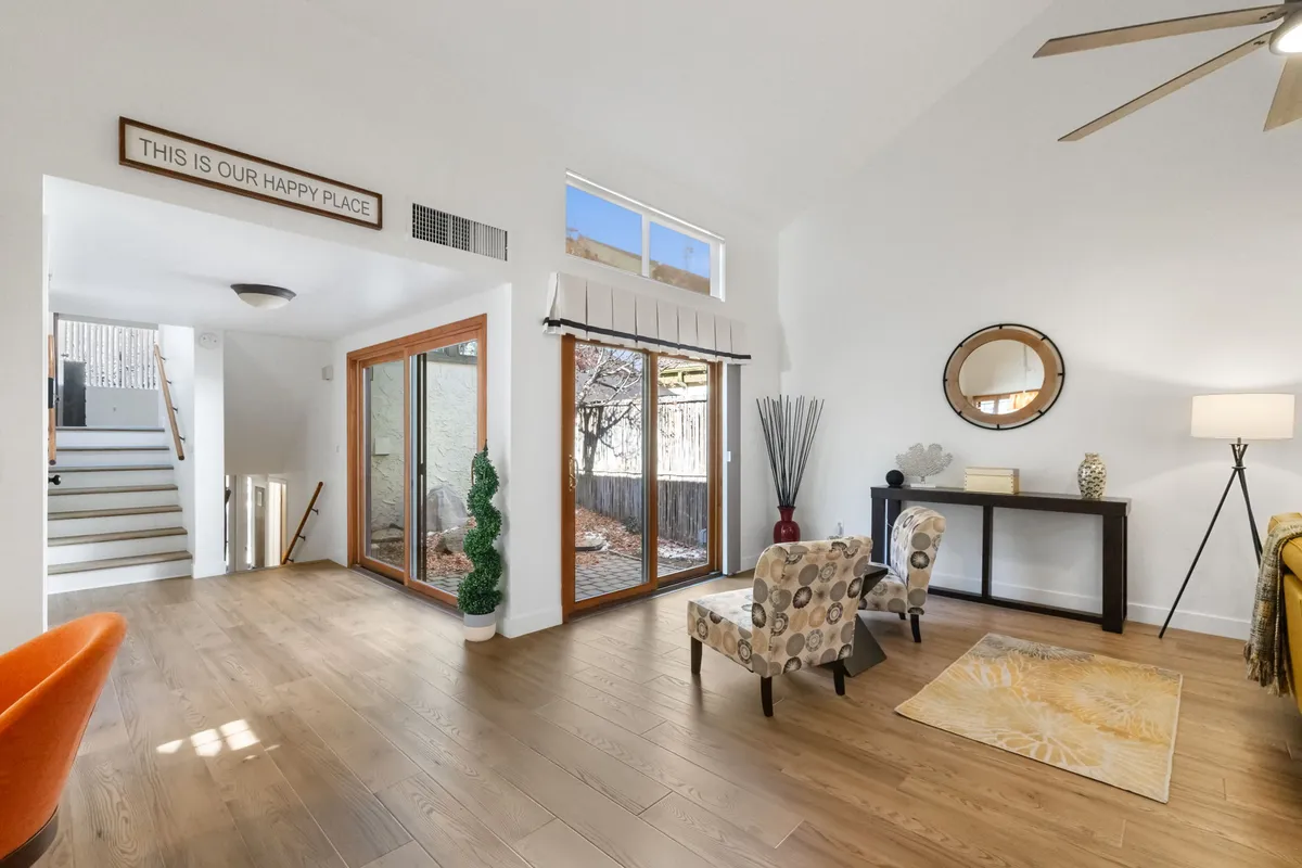 A bright, happy living area with large windows letting in natural light, stylish accent chairs, plants, and a console table with a lamp. The space is open and airy, emphasizing comfort, relaxation, and a harmonious connection with the outdoors.
