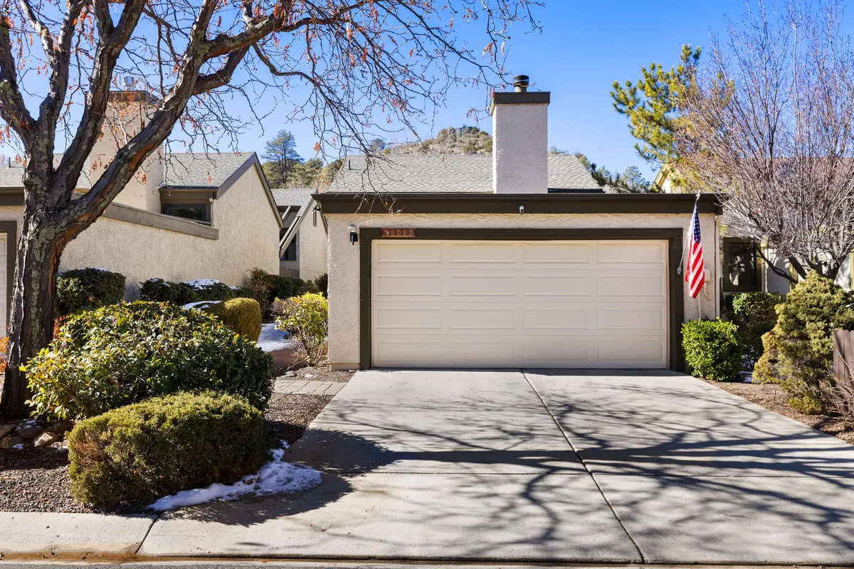This exterior image features the house’s garage door framed by welcoming landscaping and a mature tree, with a flag visible in the scene. The driveway offers a sense of arrival and a tranquil place for outdoor leisure, with morning sunlight suggesting opportunities for enjoying coffee outside.