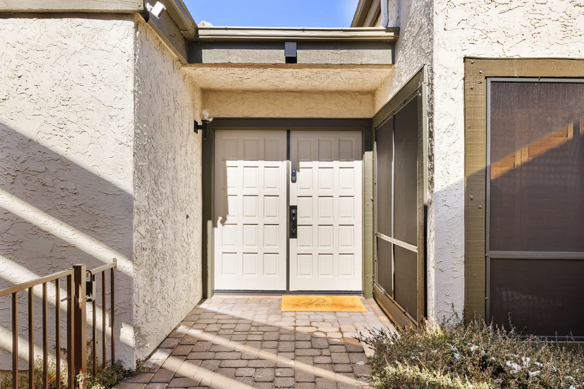 This exterior image showcases the home's double front doors, a welcoming paved pathway, and lush surrounding greenery, presenting the entrance as both inviting and memorable. The setting makes it easy to envision arriving with family or friends, ready to embark on a group getaway.