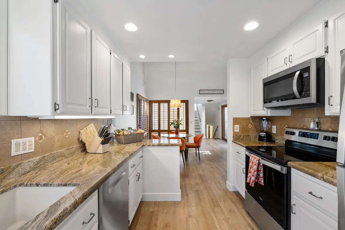 A bright, open kitchen with granite countertops, stainless steel appliances, a spacious kitchen island, and a connected dining area. Natural light streams in from a window, highlighting the inviting workspace and adjacent seating area, suggesting a space perfect for cooking, entertaining, and gathering as a group.