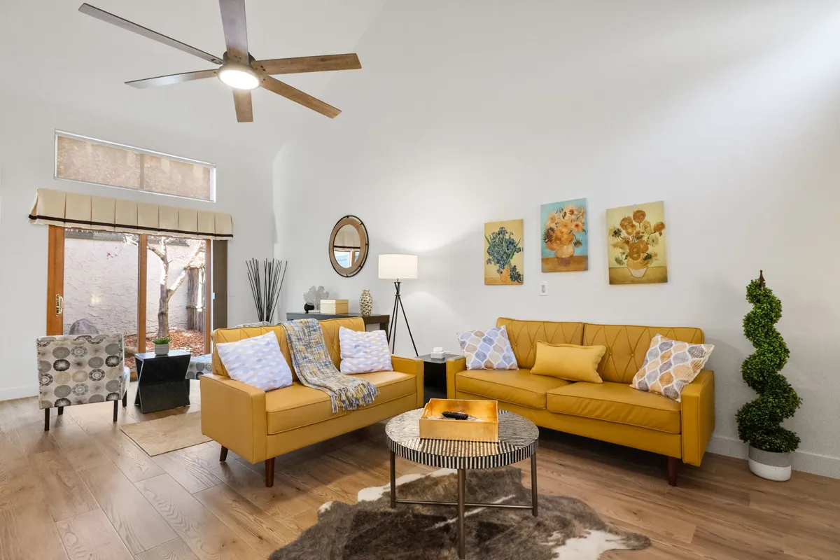 The image showcases a bright, inviting living room featuring cheerful yellow sofas, modern artwork on the wall, a sleek coffee table, and a cozy floor lamp. Natural light streams in, creating a warm and welcoming space perfect for relaxation or gathering with loved ones.