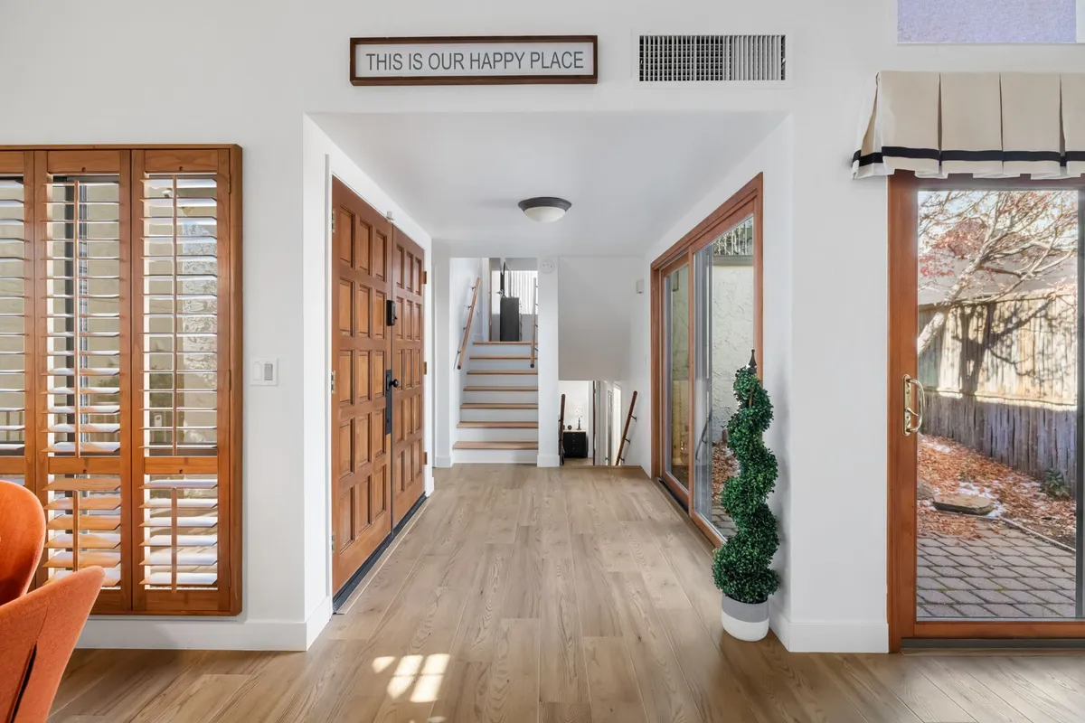 A view from the entrance highlighting the front door, staircase, and large windows that let in natural light. The space feels open and welcoming, emphasizing the layout and the sense of arrival and gathering.