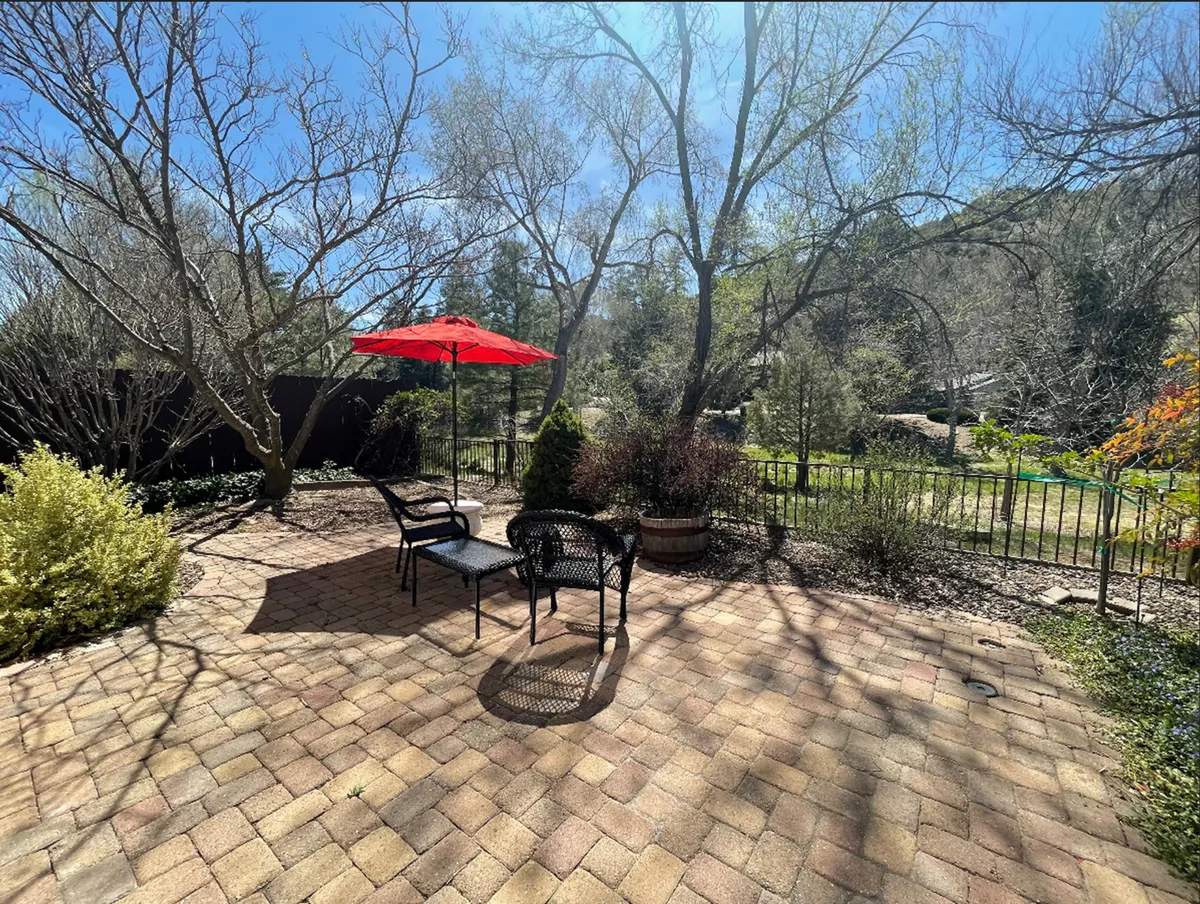 A tranquil backyard seating area with a red umbrella and black chairs set beside a landscaped garden. The setup exudes comfort and invites relaxation, reading, or meals outdoors, while showcasing the backyard as an extension of living space into nature.